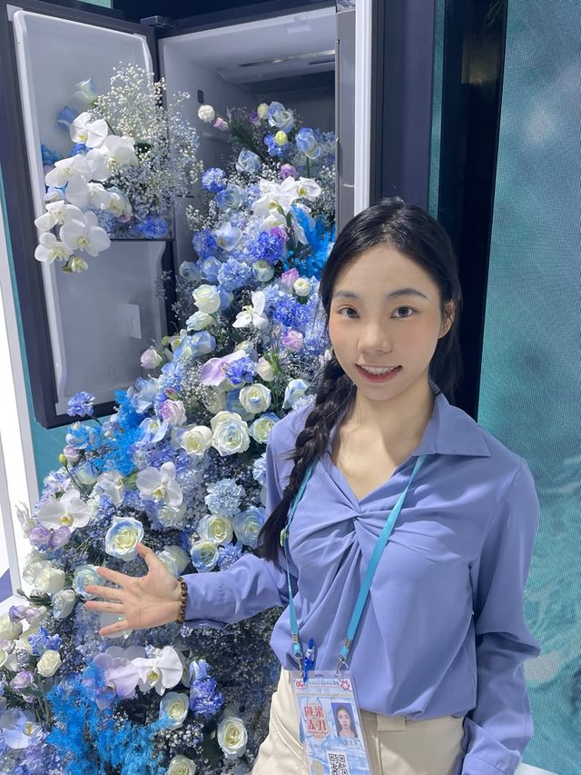 Shirley Chou beside a large display of blue and white artificial flowers at a Guangzhou exhibition stand